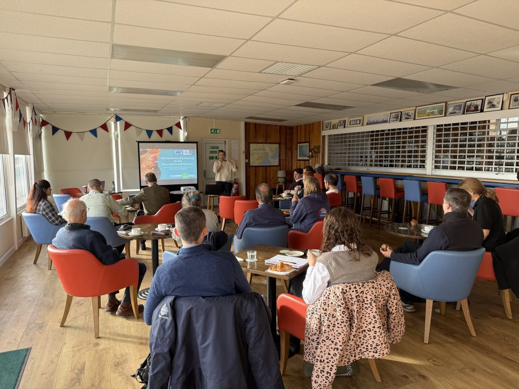 Stour & Orwell workshop A group of people seated in a marina meeting room attending a marine biosecurity workshop, viewing a presentation about invasive non‑native species and estuary protection for the Stour and Orwell Estuaries.