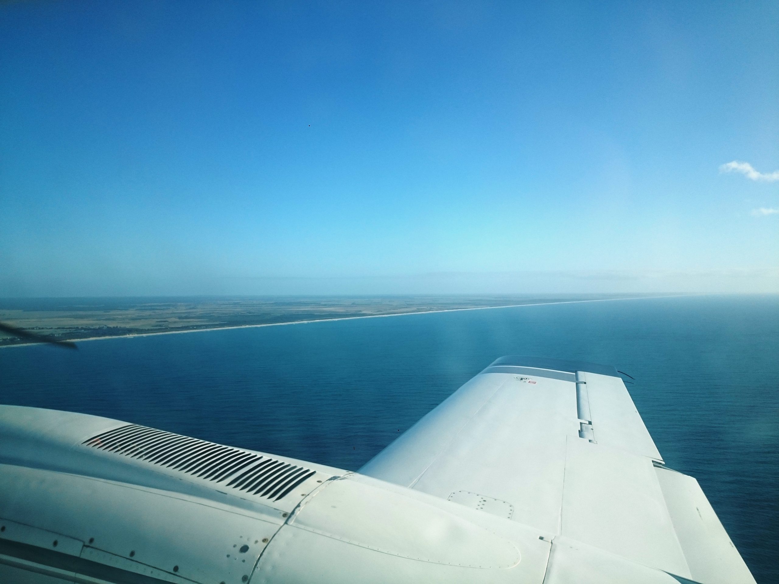 Aerial coastline survey from aircraft showing open ocean, sandy shoreline and barrier island system, supporting coastal mapping, erosion monitoring and marine environment assessment